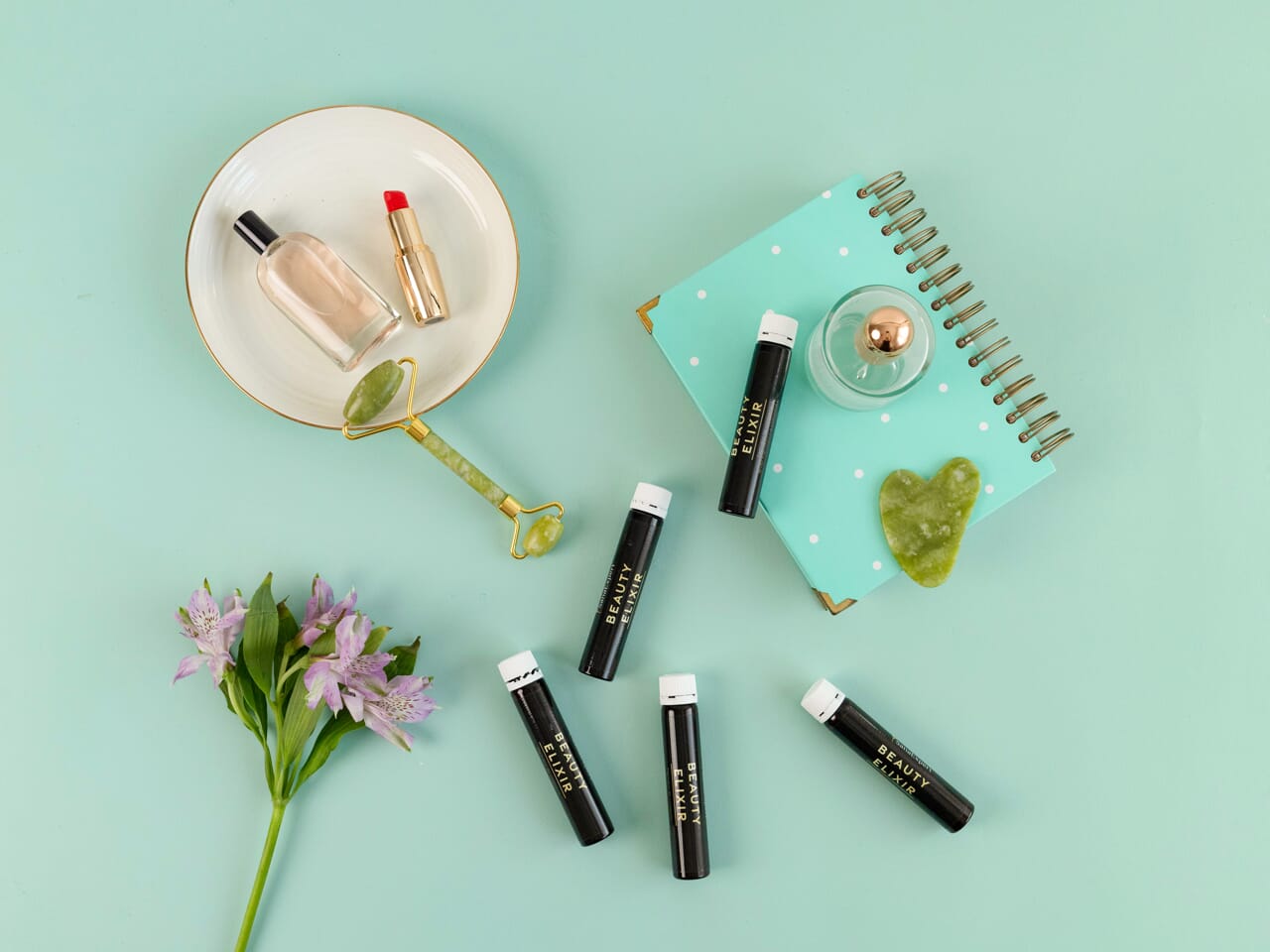 Ein flachgelegtes Set von SanaExpert Collagen Beauty Elixir Flaschen, umgeben von Schönheitsprodukten und einem Notizbuch auf türkisem Hintergrund.