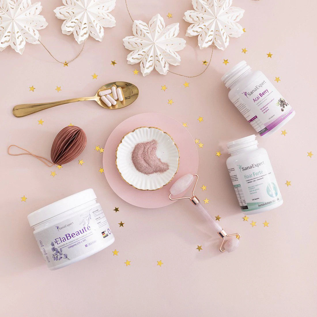 SanaExpert Haar Forte und Acai Berry Supplement-Dosen arrangiert mit Wellness-Utensilien wie einem Honiglöffel und einem Gesichtsroller auf einem sanft rosafarbenen Hintergrund, dekoriert mit zarten Schneeflocken-Dekorationen.