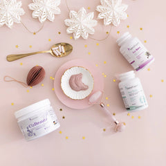 SanaExpert Haar Forte und Acai Berry Supplement-Dosen arrangiert mit Wellness-Utensilien wie einem Honiglöffel und einem Gesichtsroller auf einem sanft rosafarbenen Hintergrund, dekoriert mit zarten Schneeflocken-Dekorationen.